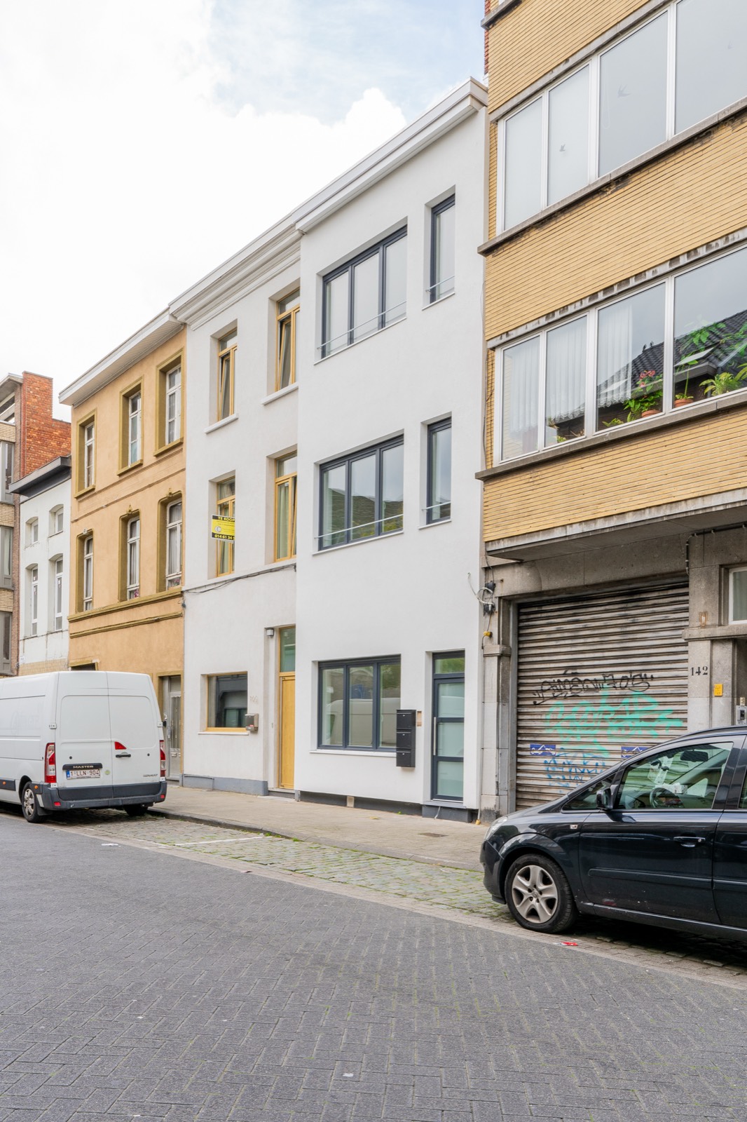 Vernieuwde witgepleisterde gevel van een Antwerpse stadswoning met donkere raamprofielen