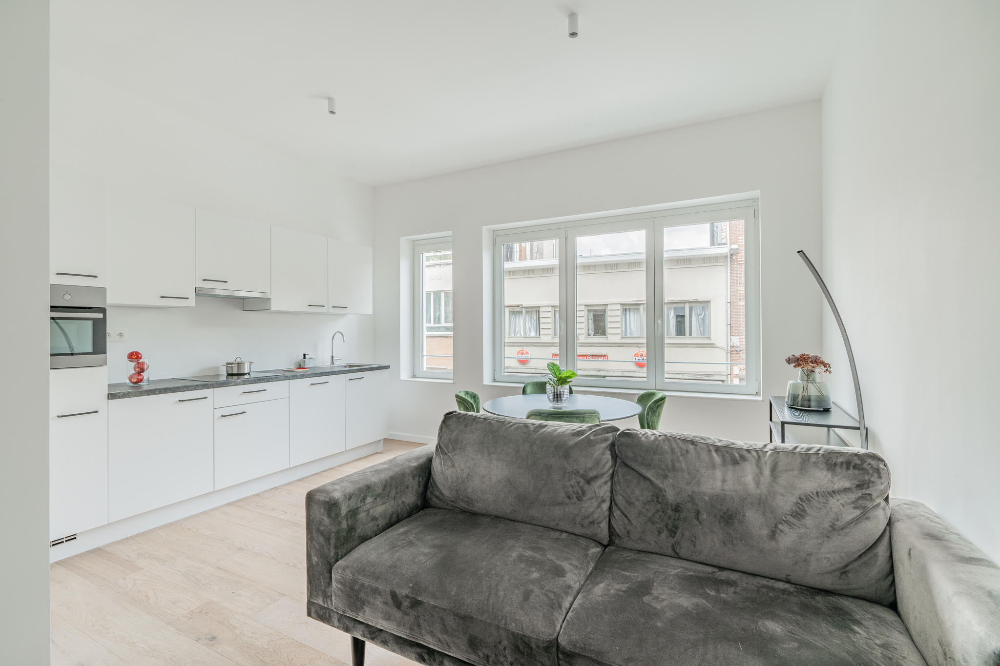 Open leefruimte met witte keuken, eettafel en zithoek met groene fluwelen stoelen